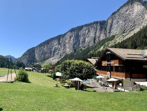 Eine Berglodge mit Außenbestuhlung und Bar, umgeben von üppiger Vegetation und einem steilen Berghintergrund.