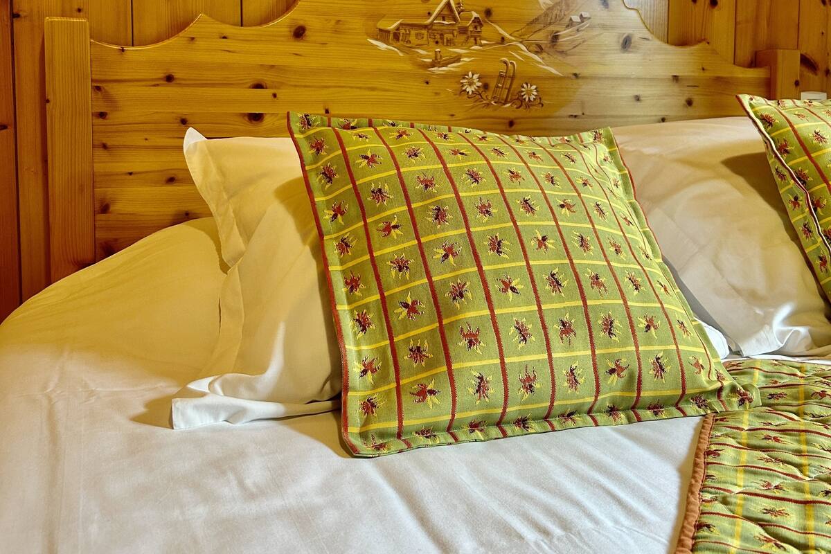 Un lit en bois avec une tête de lit sculptée, une literie blanche et des coussins à motifs verts.