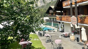 A bar restaurant with outdoor seating, a mountain backdrop, and a sign indicating it is a hotel restaurant. - Hameau des Prodains - Hôtel (Morzine)
