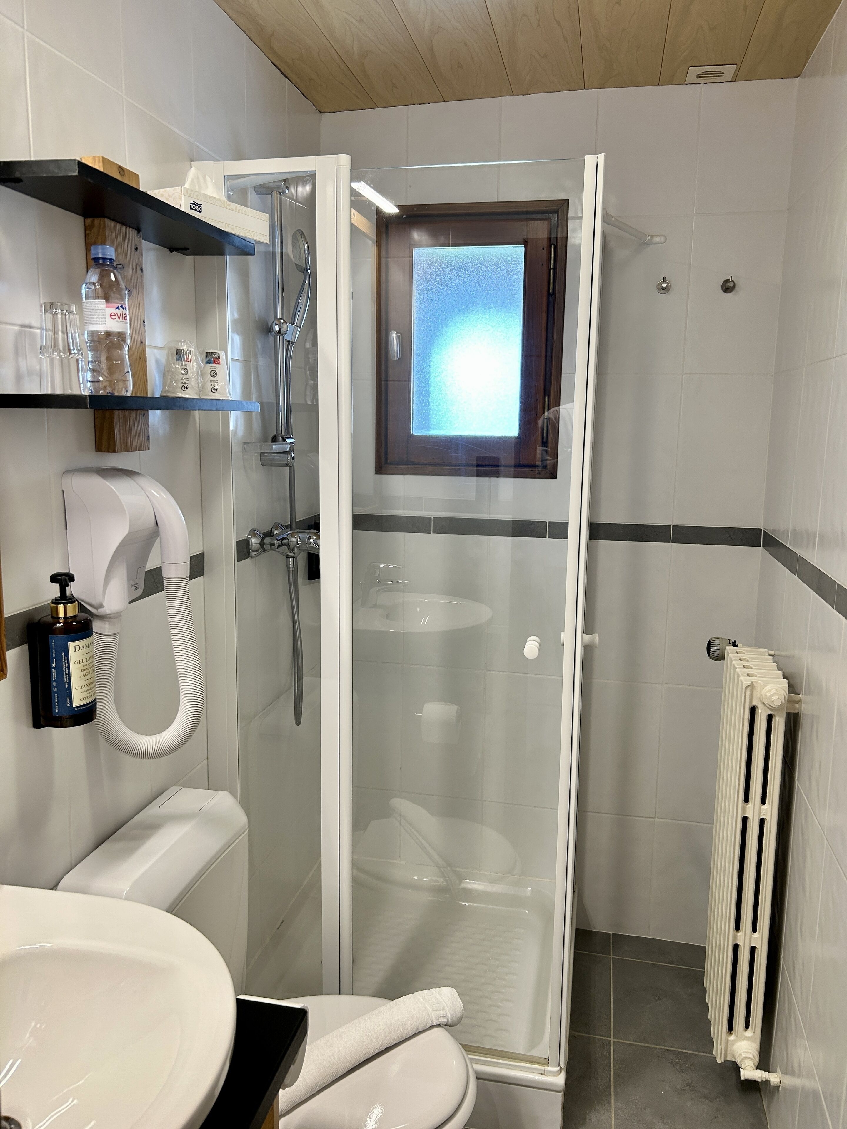 Un baño moderno con ducha de vidrio, inodoro blanco, lavabo y toallero.