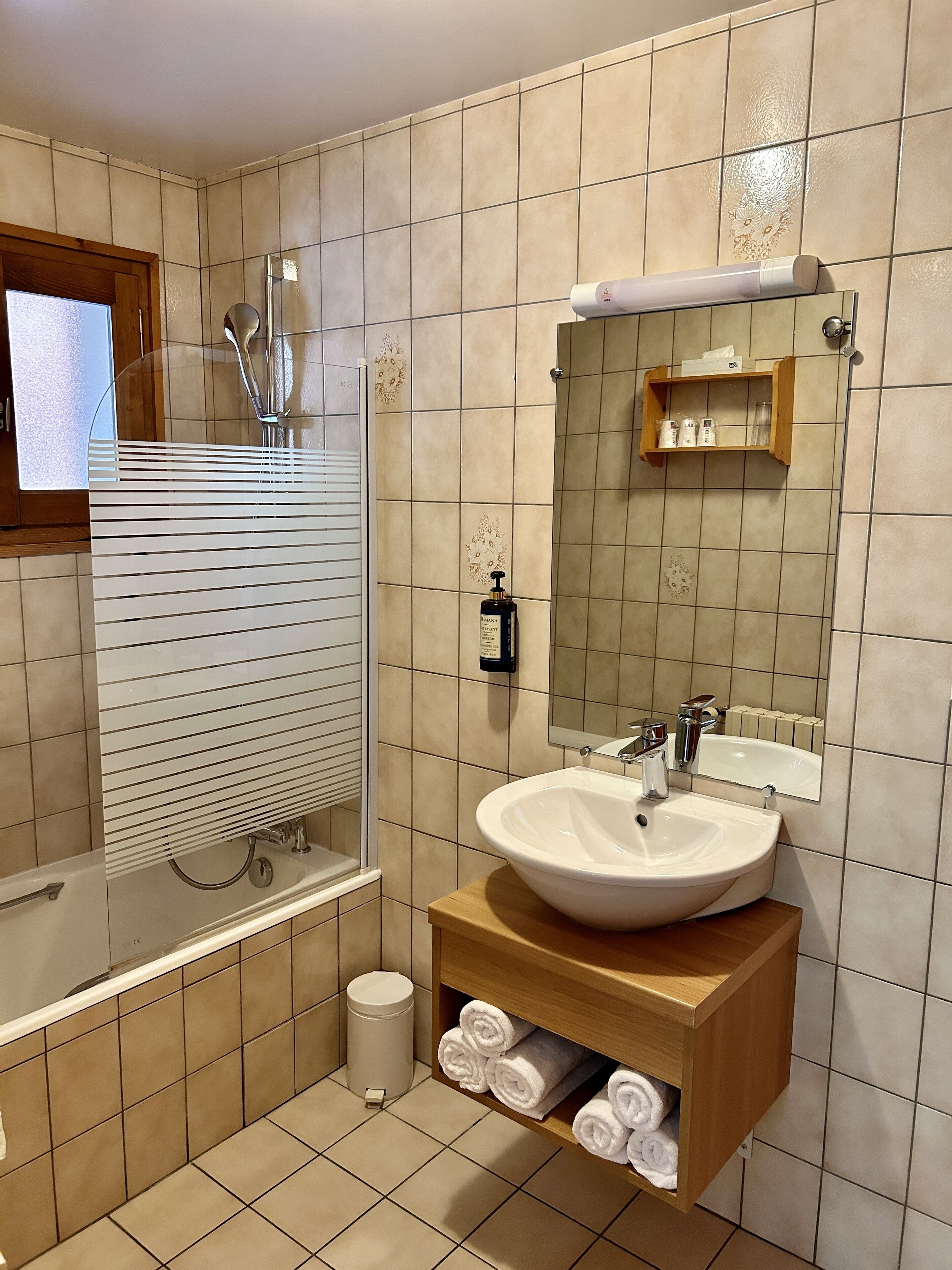 A bathroom with a bathtub, a sink, a mirror, and a shelf with towels.