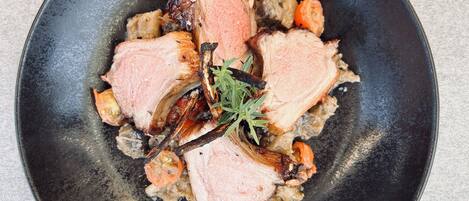 Une assiette noire contenant de la viande tranchée, des légumes et une branche de romarin.