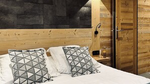 A bedroom with a wooden headboard, a dark wall, a bedside table with a bottle, and a wardrobe. - Hameau des Prodains - Hôtel (Morzine)