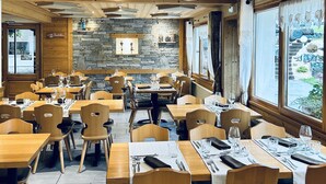 A restaurant with wooden tables and chairs, stone walls, and a view of the outdoors. - Hameau des Prodains - Hôtel (Morzine)