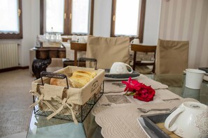 Una mesa de comedor con un cesto de pan, una rosa roja y una bandeja con una taza blanca.
