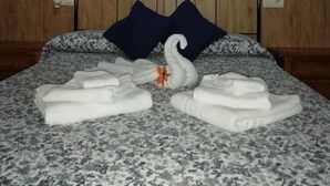 A neatly made bed with a floral-patterned bedspread, two pillows, and a decorative swan made of towels. - Hostal Breñaverde (Gaucin)