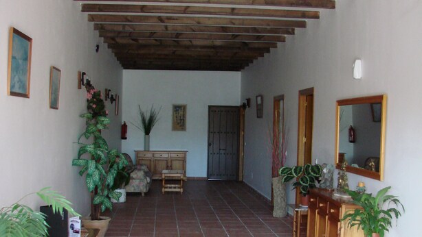 A spacious hallway with tiled flooring, wooden furniture, and potted plants. - Hostal Breñaverde (Gaucin)