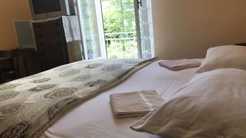Un lit bien fait, recouvert d’une couvre-lit à motifs floraux, un téléviseur posé sur un meuble, et une fenêtre donnant sur un paysage verdoyant.