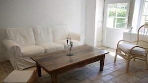 A living room with a wooden coffee table, white sofa, wicker chair, and a small wooden chest. - La Ferme les Eybrachas (Réauville)