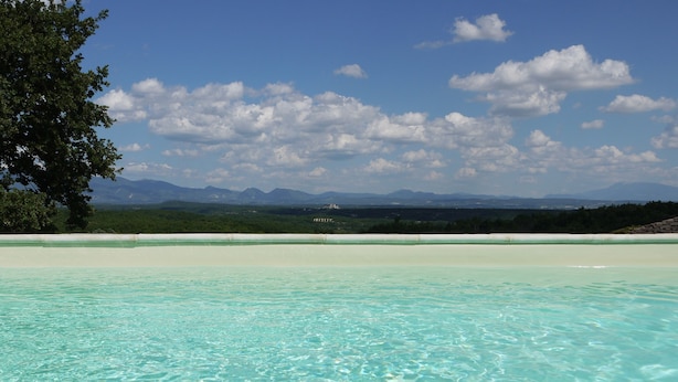 A clear turquoise pool with a view of distant mountains and a tree-lined horizon. - La Ferme les Eybrachas (Réauville)