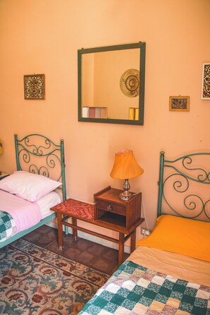 A room with two beds, a nightstand, a lamp, and a mirror on the wall. - Casa Verdi (Catania)