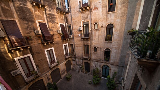 A courtyard with multiple buildings, balconies, and potted plants. - Casa Verdi (Catania)