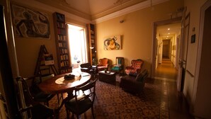 A cozy living room with a round wooden table, comfortable seating, a bookshelf, and a painting on the wall. - Casa Verdi (Catania)