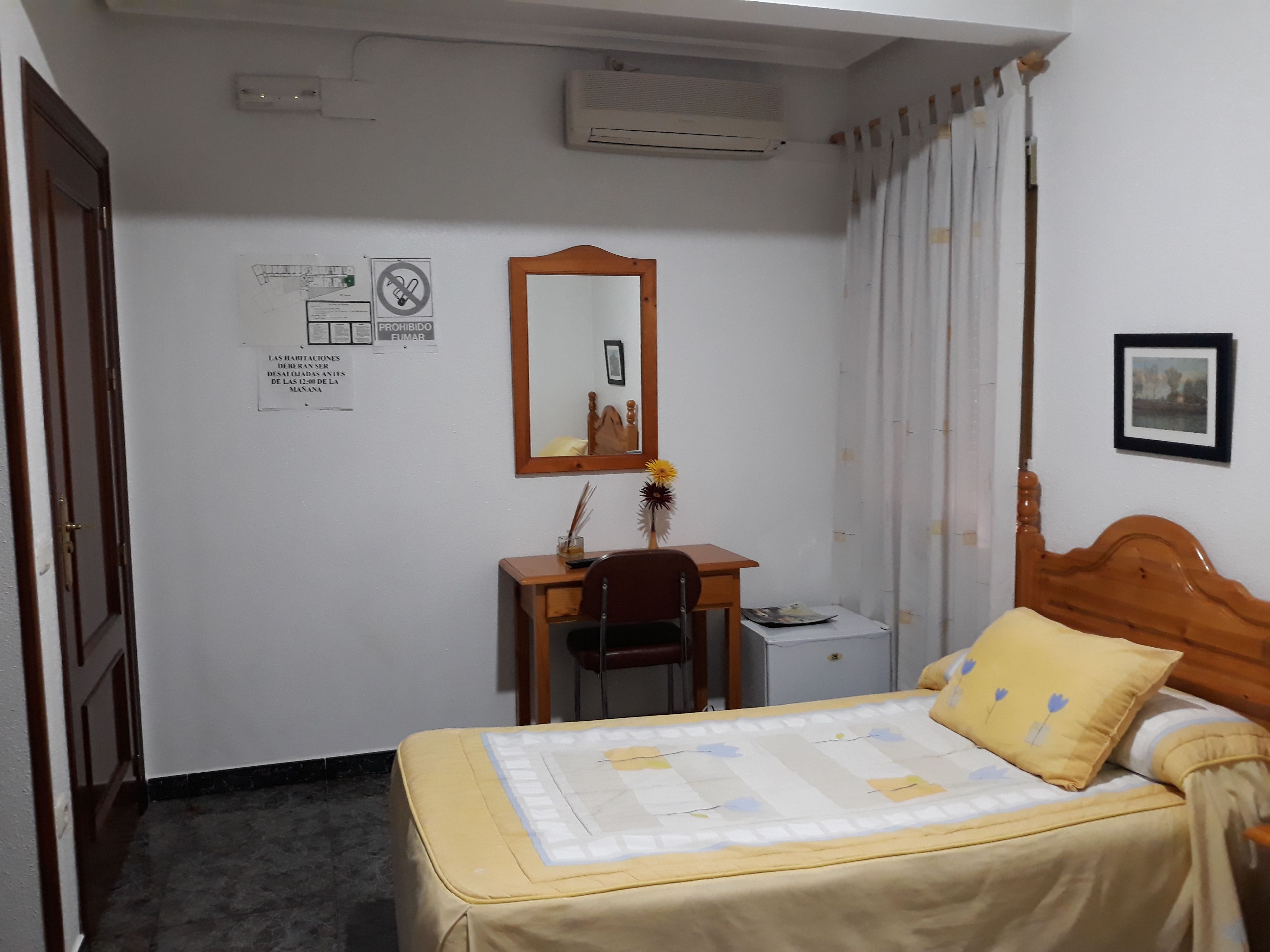 Una camera da letto con un letto, una scrivania, una sedia, uno specchio e un quadro appeso al muro.