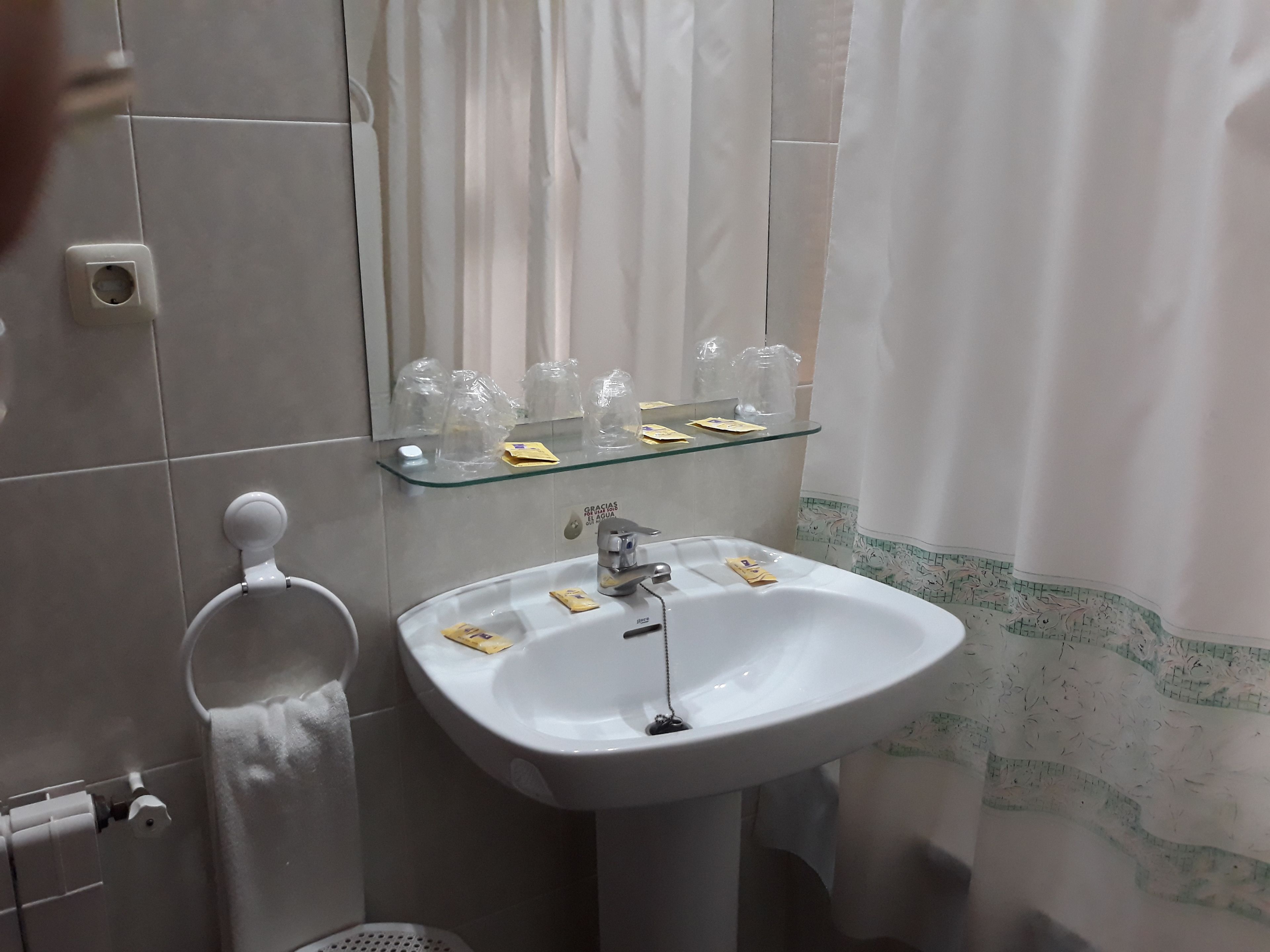 A bathroom with a white sink, a glass shelf above it, a towel rack, and a shower curtain.