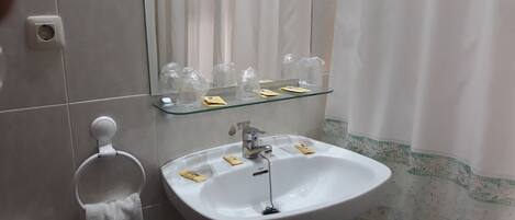 A bathroom with a white sink, a glass shelf above it, a towel rack, and a shower curtain.