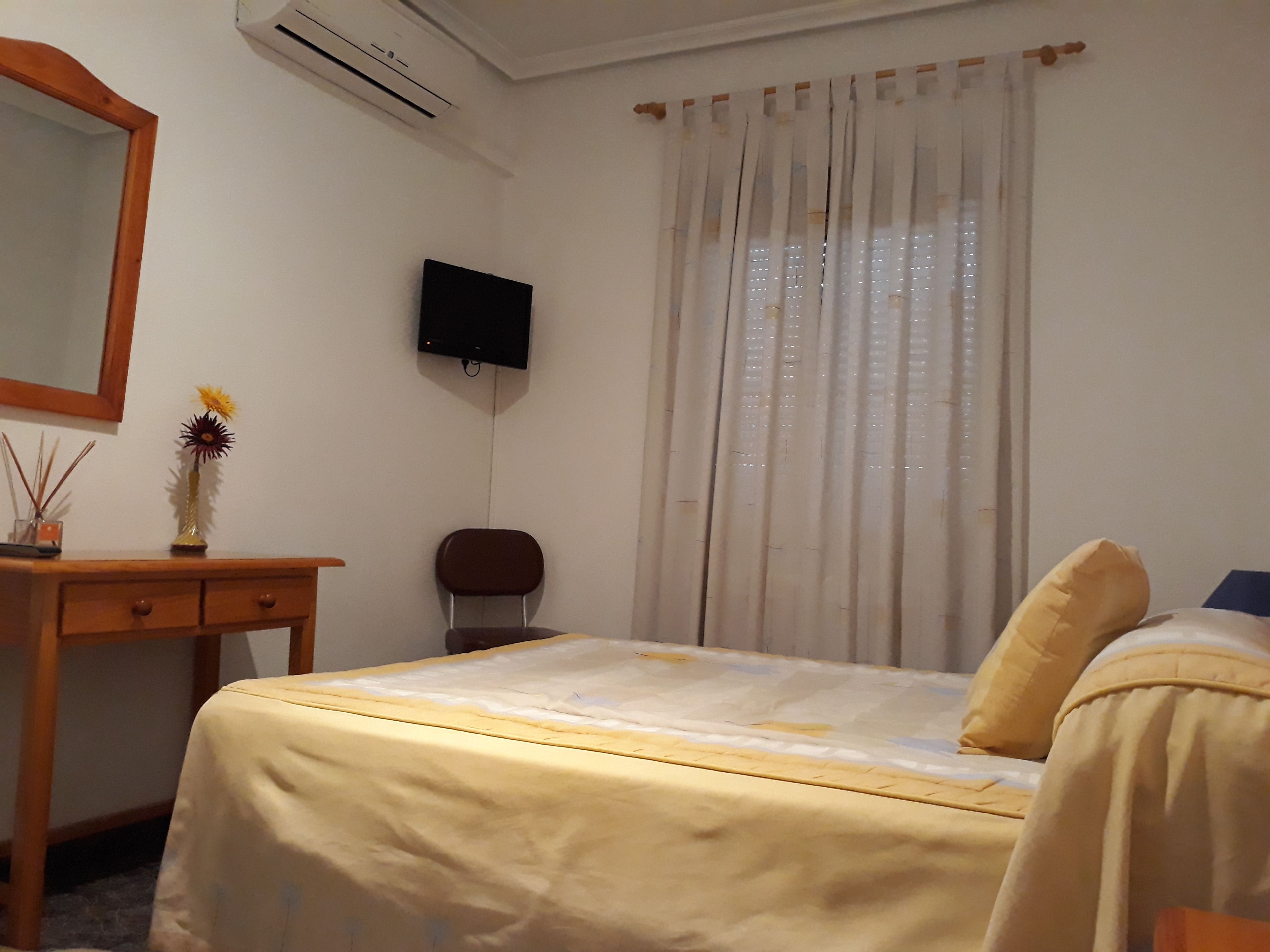 Une chambre d’hôtel équipée d’un lit, d’un bureau, d’une chaise, d’un téléviseur fixé au mur et d’une fenêtre avec des rideaux.