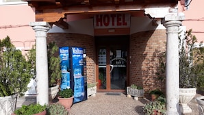 Entrada de hotel con un letrero que dice "HOTEL" sobre la puerta. A ambos lados de la entrada hay dos máquinas expendedoras de agua con la marca "Valtorre".