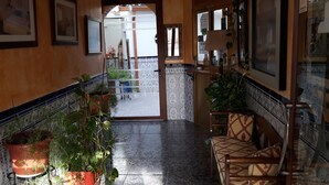 Un pasillo con plantas en macetas, una silla de madera y piso de baldosas.