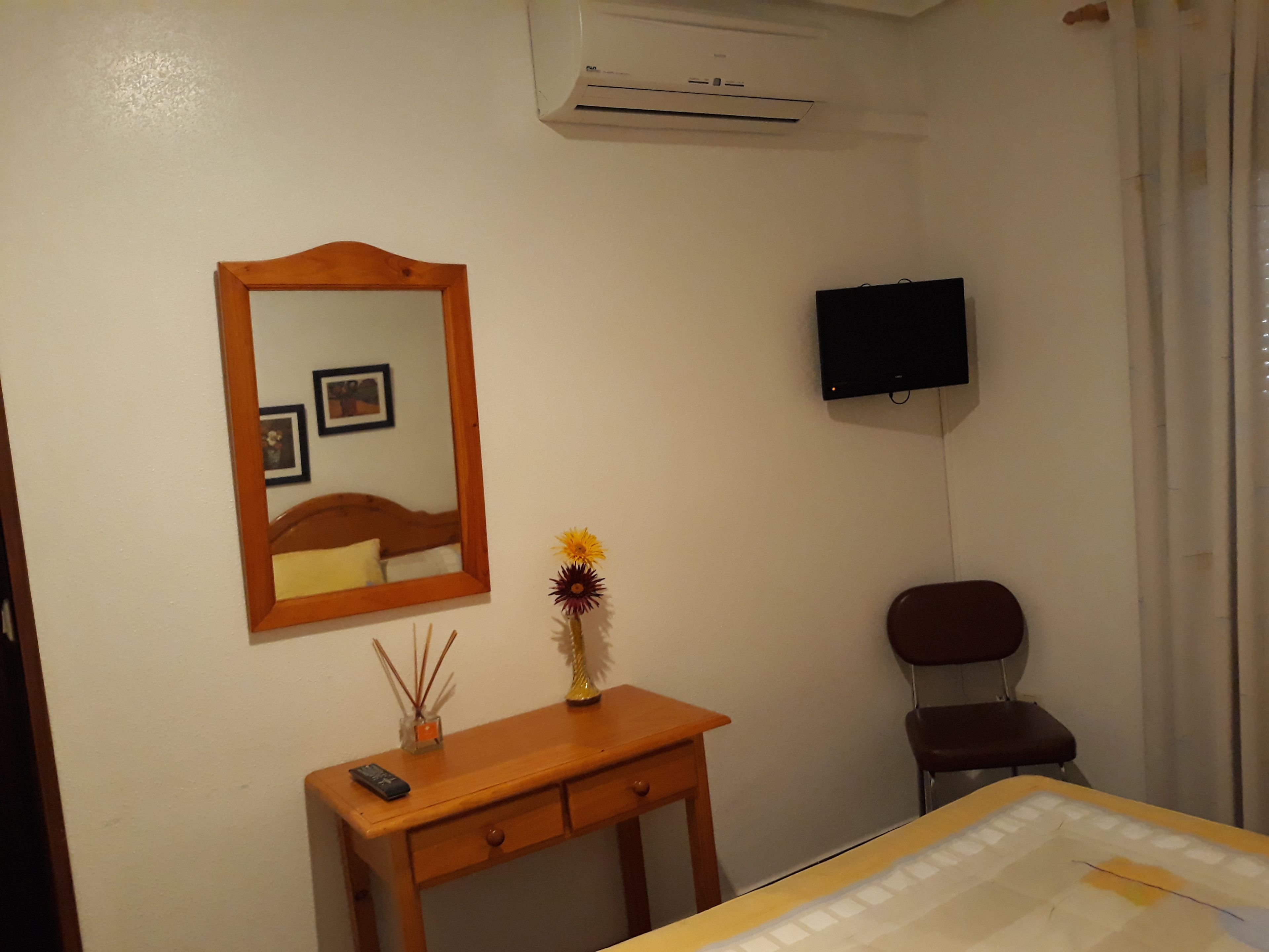 A bedroom with a bed, a wooden dresser, a mirror, a television, and a chair.
