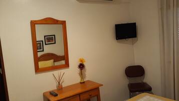 A bedroom with a bed, a wooden dresser, a mirror, a television, and a chair.
