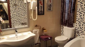A bathroom with a sink, toilet, and bathtub. There are towels and a small table with a vase.