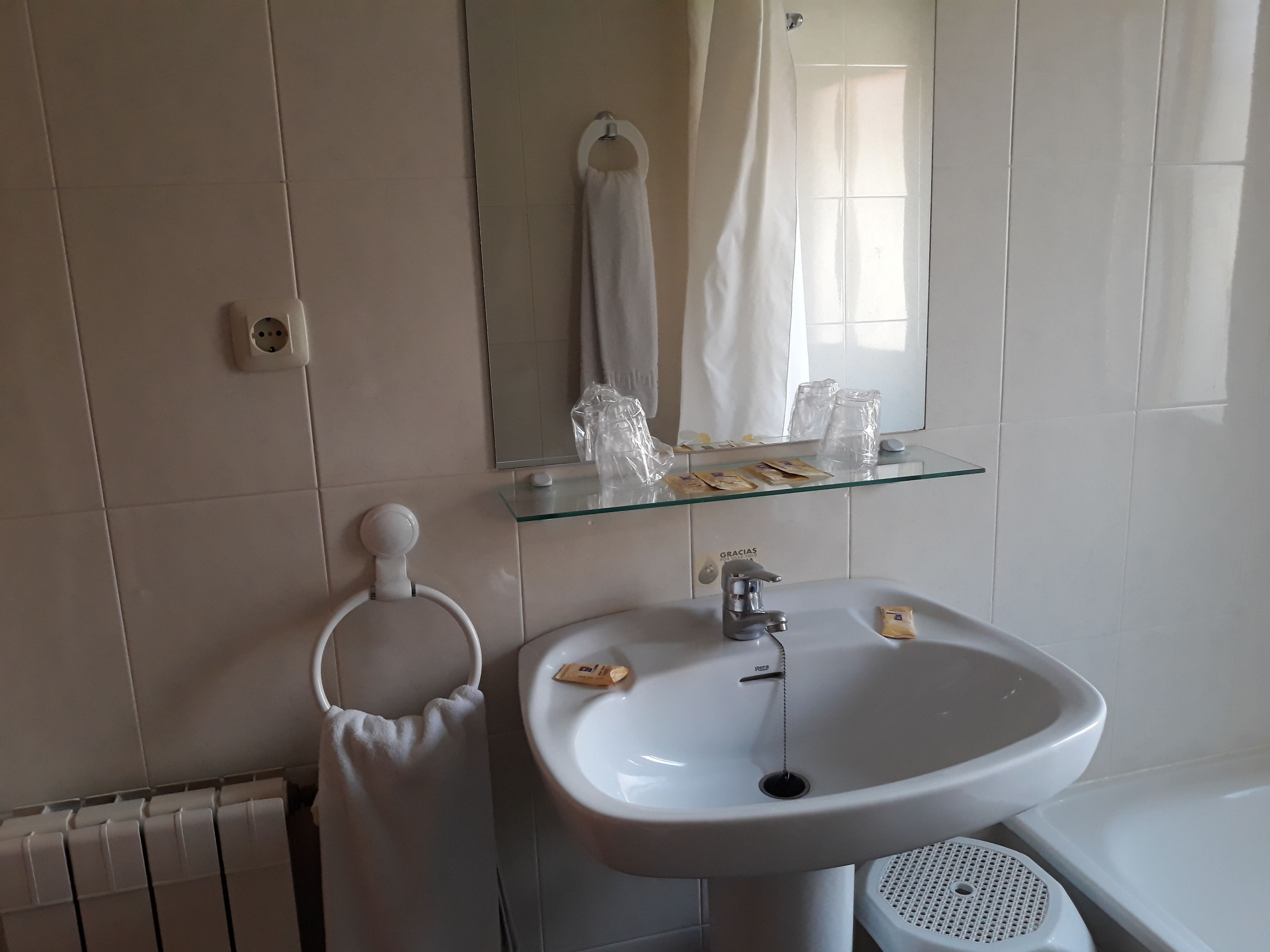 A bathroom with a white sink, a mirror, a towel rack, and a glass shelf with toiletries.