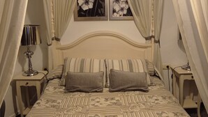 Un dormitorio con cama, dos almohadas, una mesita de noche con lámpara y un cuadro en la pared.