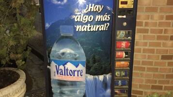 Un distributeur d’eau Valtorre, orné d’une publicité représentant un paysage naturel, est installé à l’extérieur, près d’un mur de briques.