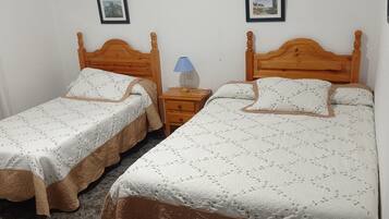 Una habitación con dos camas de madera, cada una con cabecera y piecera a juego. Entre las camas, una mesita de noche con una lámpara.