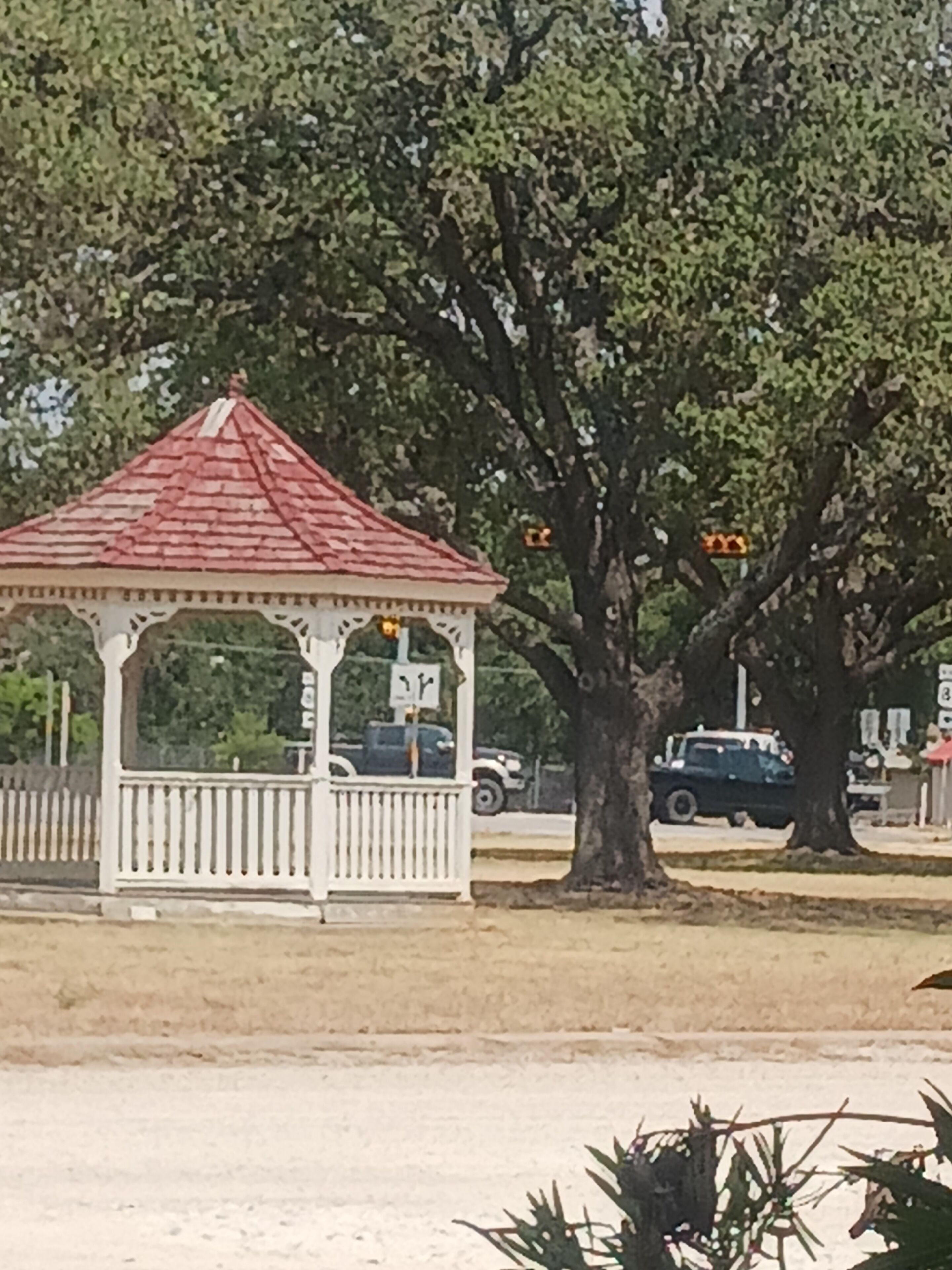 A gazebo with a red roof and white columns, surrounded by trees and a fence.