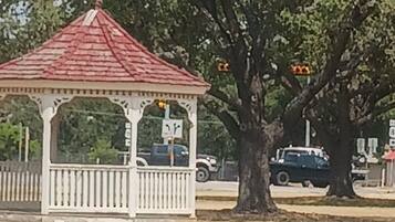 A gazebo with a red roof and white columns, surrounded by trees and a fence.