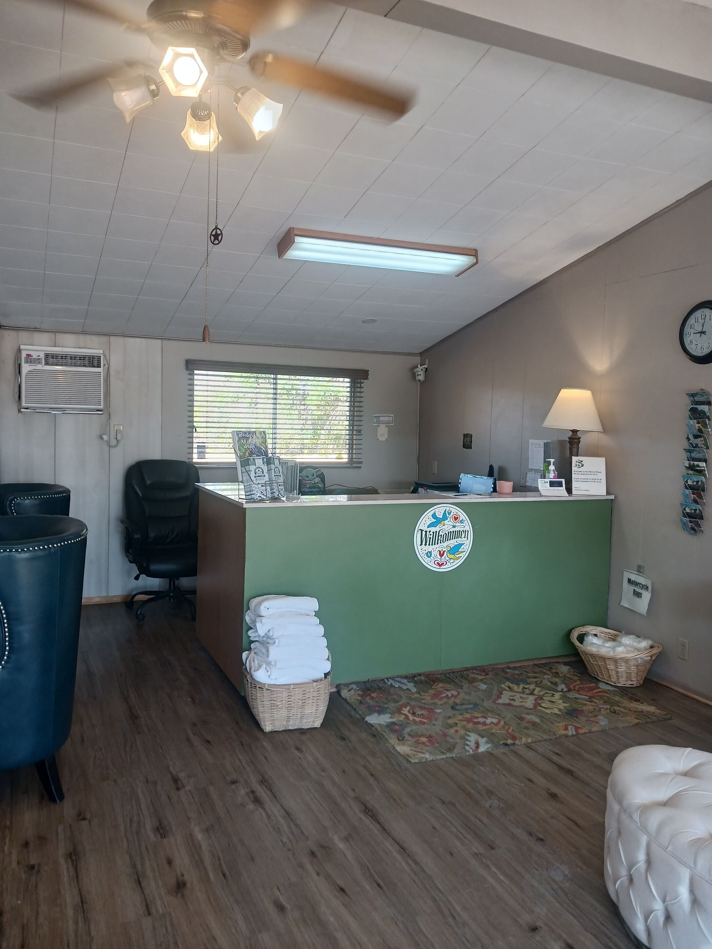 A reception area with a green counter, a black office chair, a ceiling fan, and a clock on the wall.