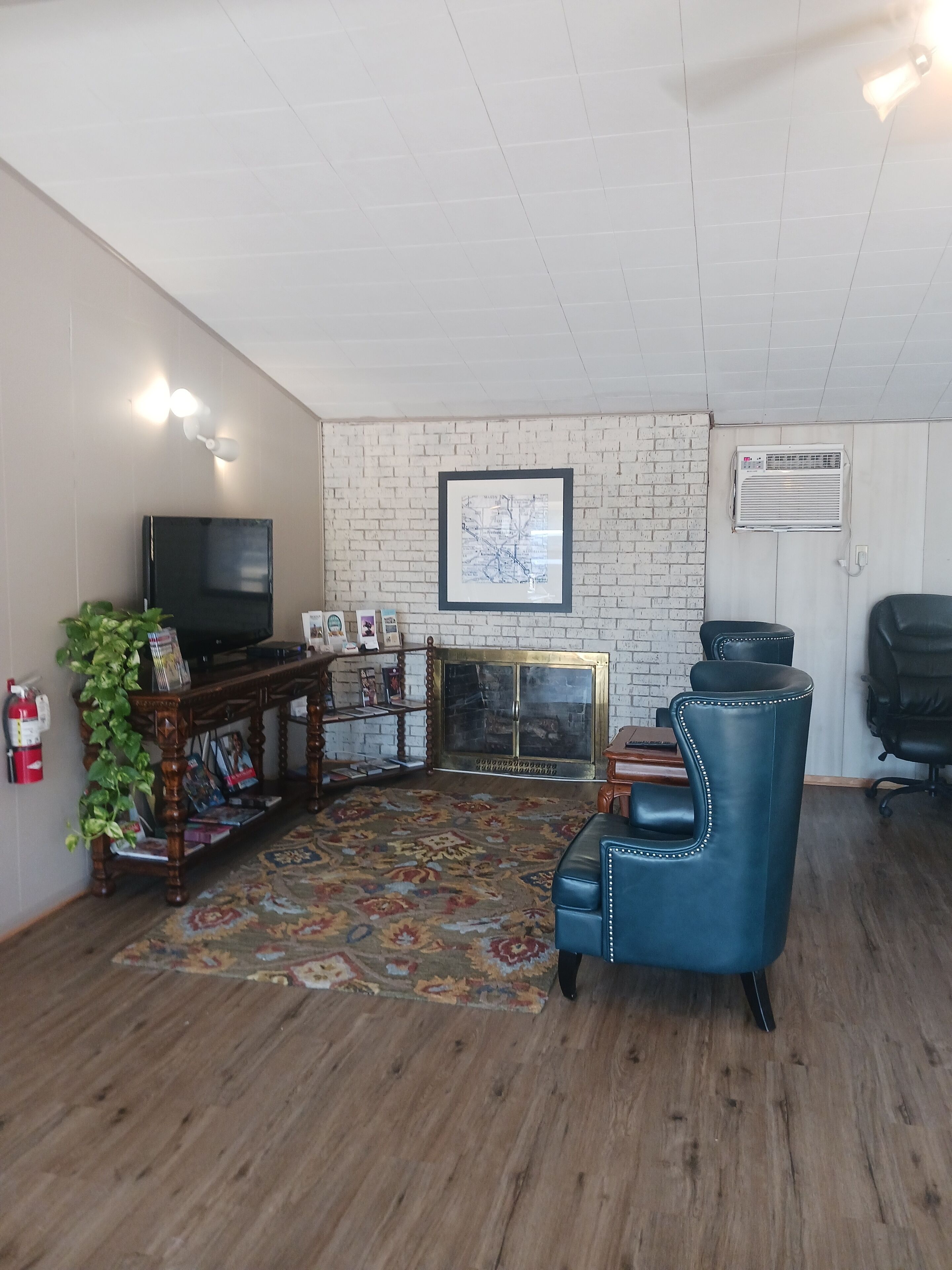 Un salon avec un téléviseur, une carte encadrée accrochée au mur, une cheminée, un fauteuil en cuir bleu et un plancher en bois.