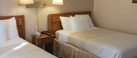 A hotel room with two beds, each with a white quilted bedspread, a wooden headboard, and a bedside table with a lamp.