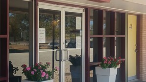 Una cafetería con puerta de cristal, zona de mesas al aire libre y macetas con flores.