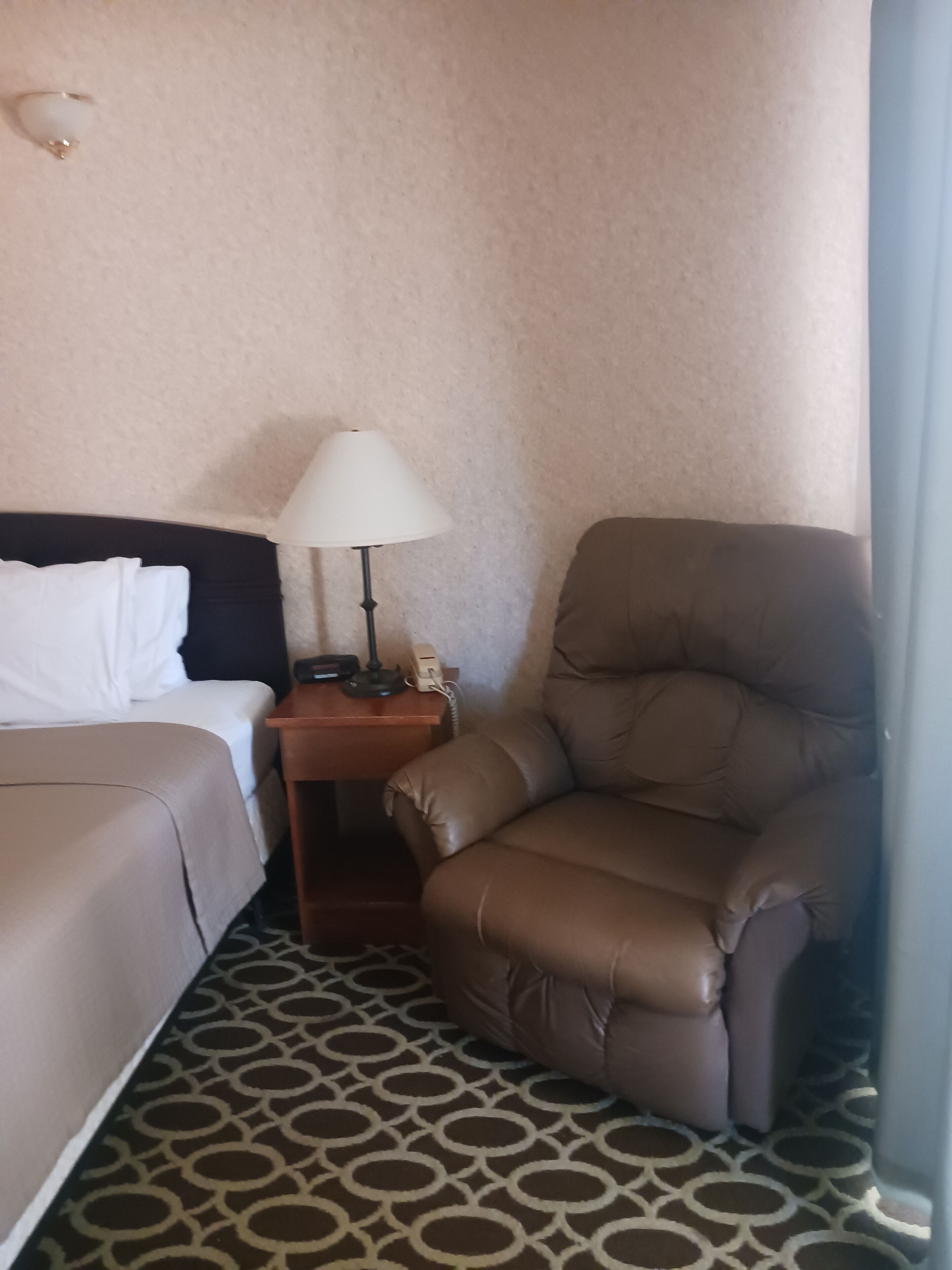 A hotel room with a bed, a desk with a lamp, and a leather armchair.