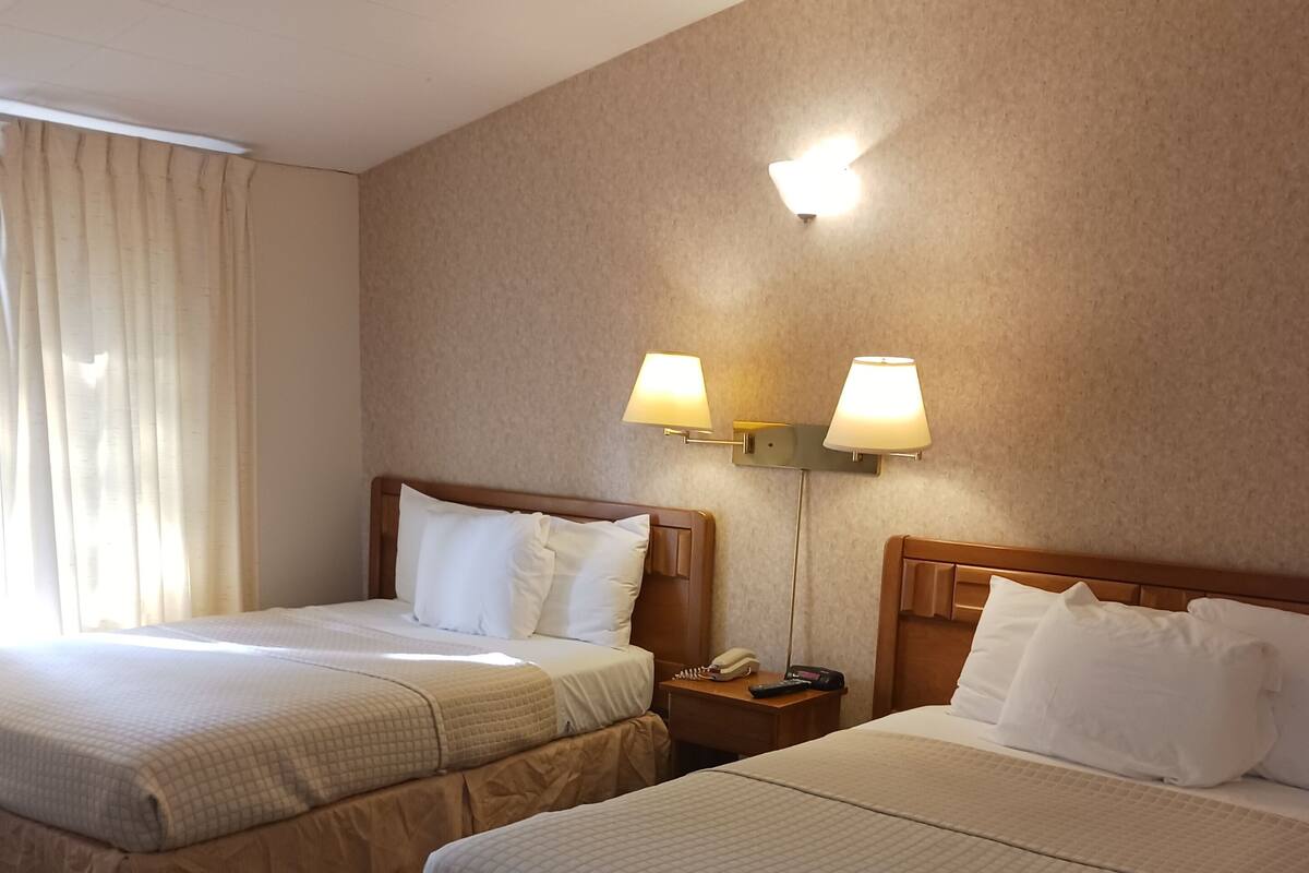A hotel room with two beds, a patterned carpet, and two wall-mounted lamps.