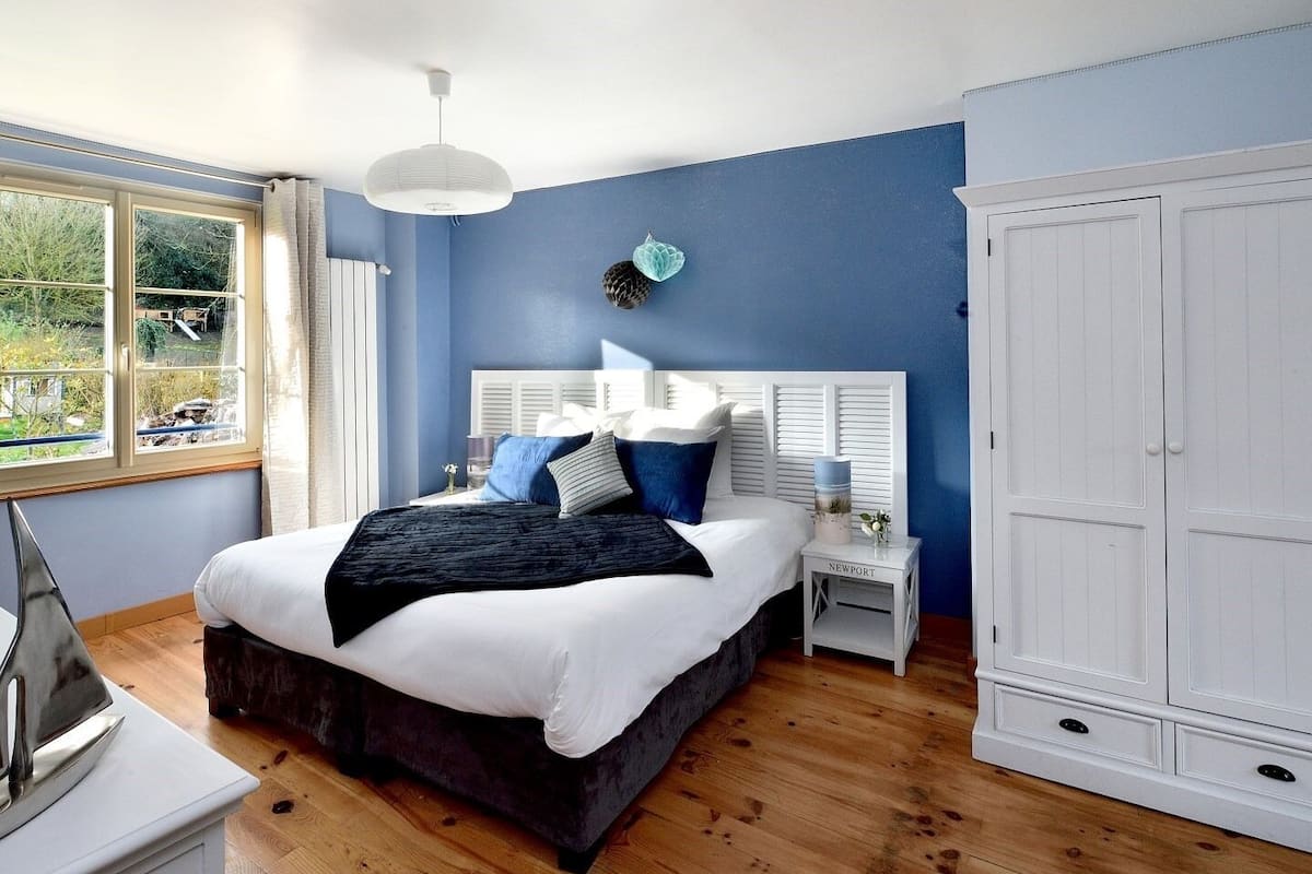 A bedroom with a large bed, a white wardrobe, a nightstand, and a window with curtains.