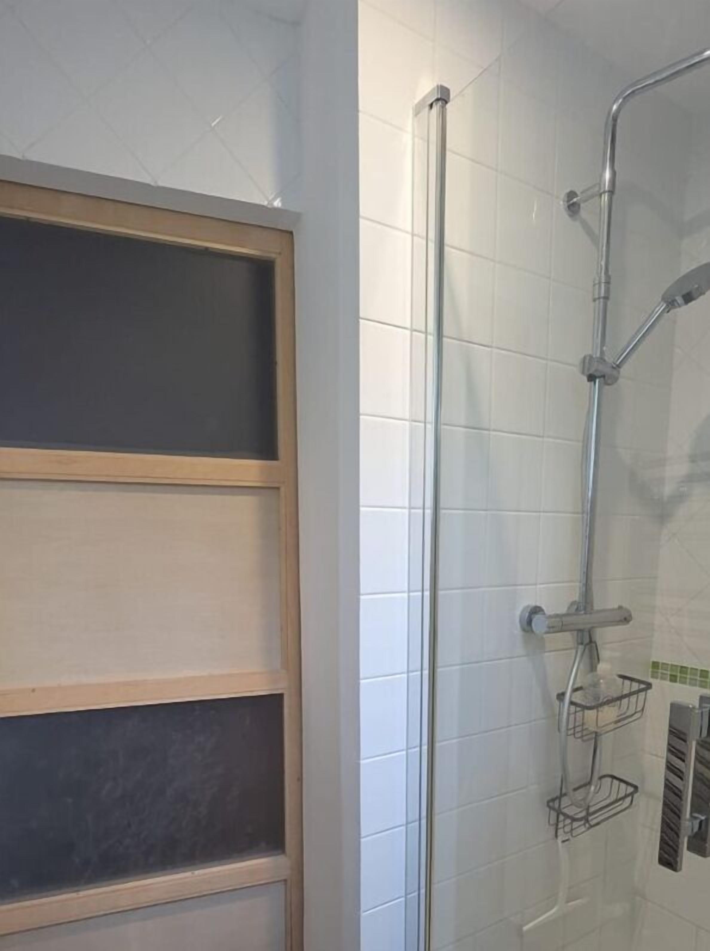 Una ducha con puerta de vidrio, ducha de metal y un pequeño estante.