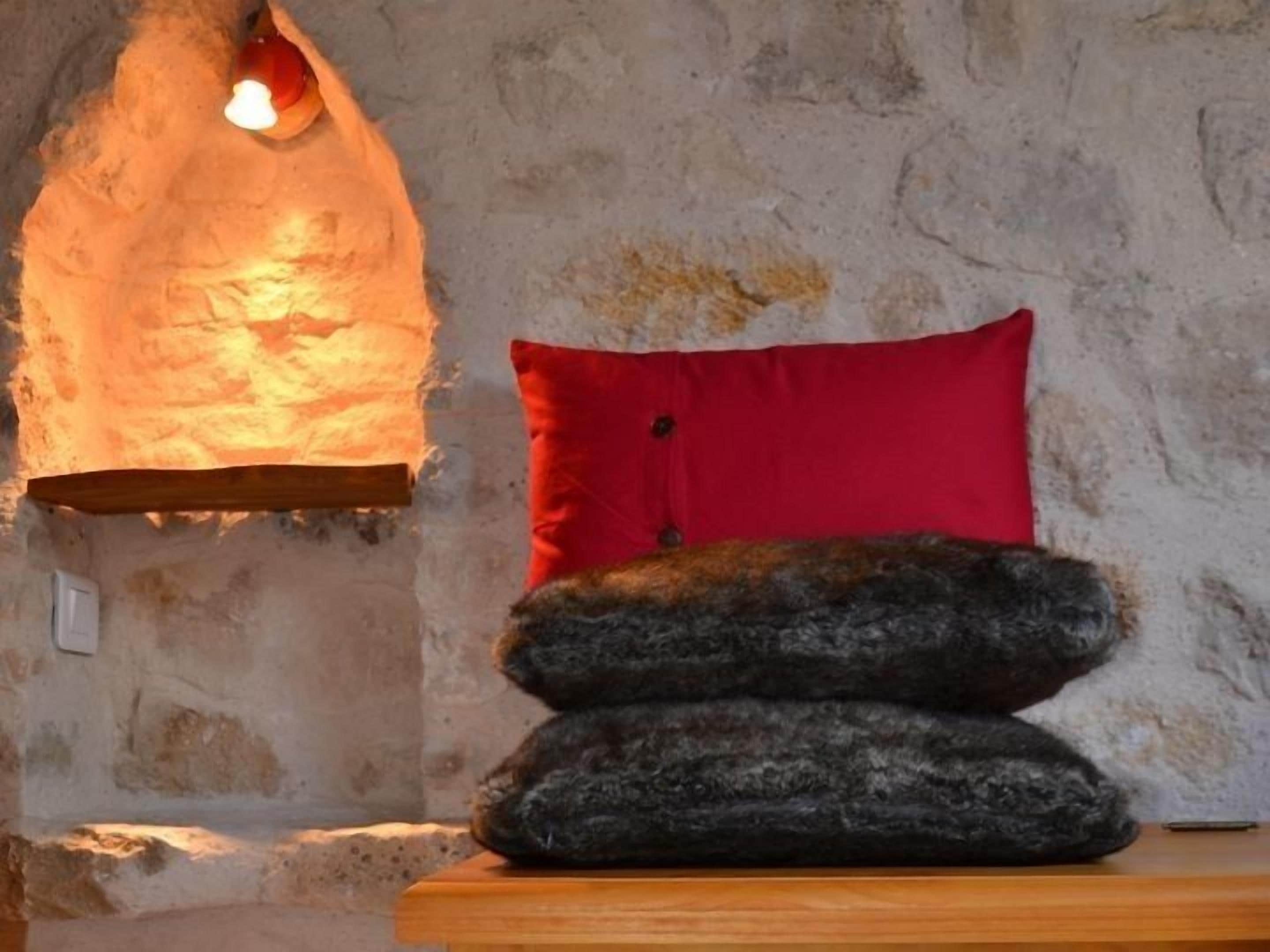 Een rustieke kamer met een stenen muur, een rood kussen en een houten bank.