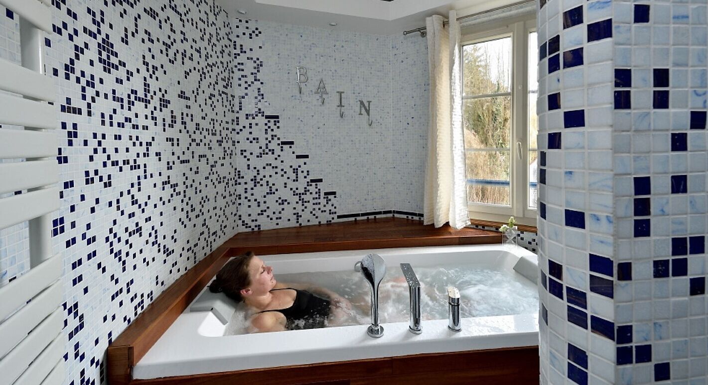 Ein Badezimmer mit mosaikbesetzter Wand, einer Badewanne und einem Fenster mit Blick auf Bäume.