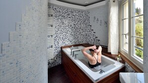 A bathroom with a freestanding bathtub, a window with a view of greenery, and a tiled wall with a pattern. - Chambres D'hôtes Villa de Vienne-en-arthies (Vienne-en-Arthies)