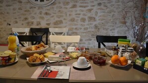 A breakfast table set with various food items, a clock on the wall, and a stone wall background. - Chambres D'hôtes Villa de Vienne-en-arthies (Vienne-en-Arthies)