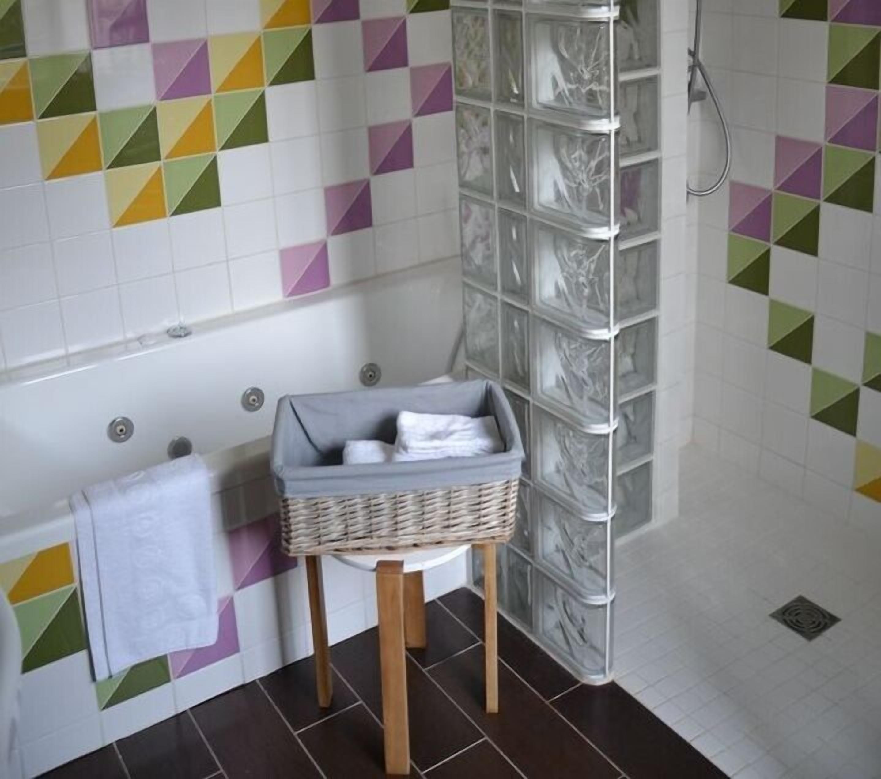 A bathroom with a tiled wall featuring geometric patterns, a white towel hanging on a rack, and a wicker basket on a wooden stool.