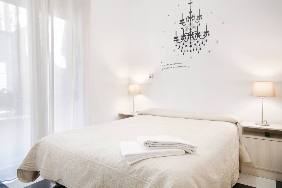 A neatly made bed with a folded towel, a chandelier wall decoration, and two bedside lamps in a hotel room.