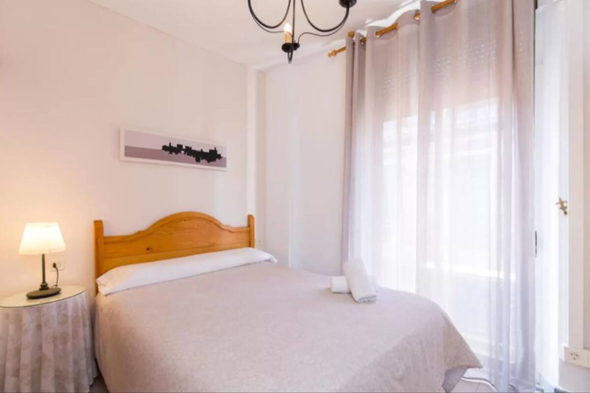 A neatly made bed with a wooden headboard, a bedside lamp, and a wall-mounted artwork.