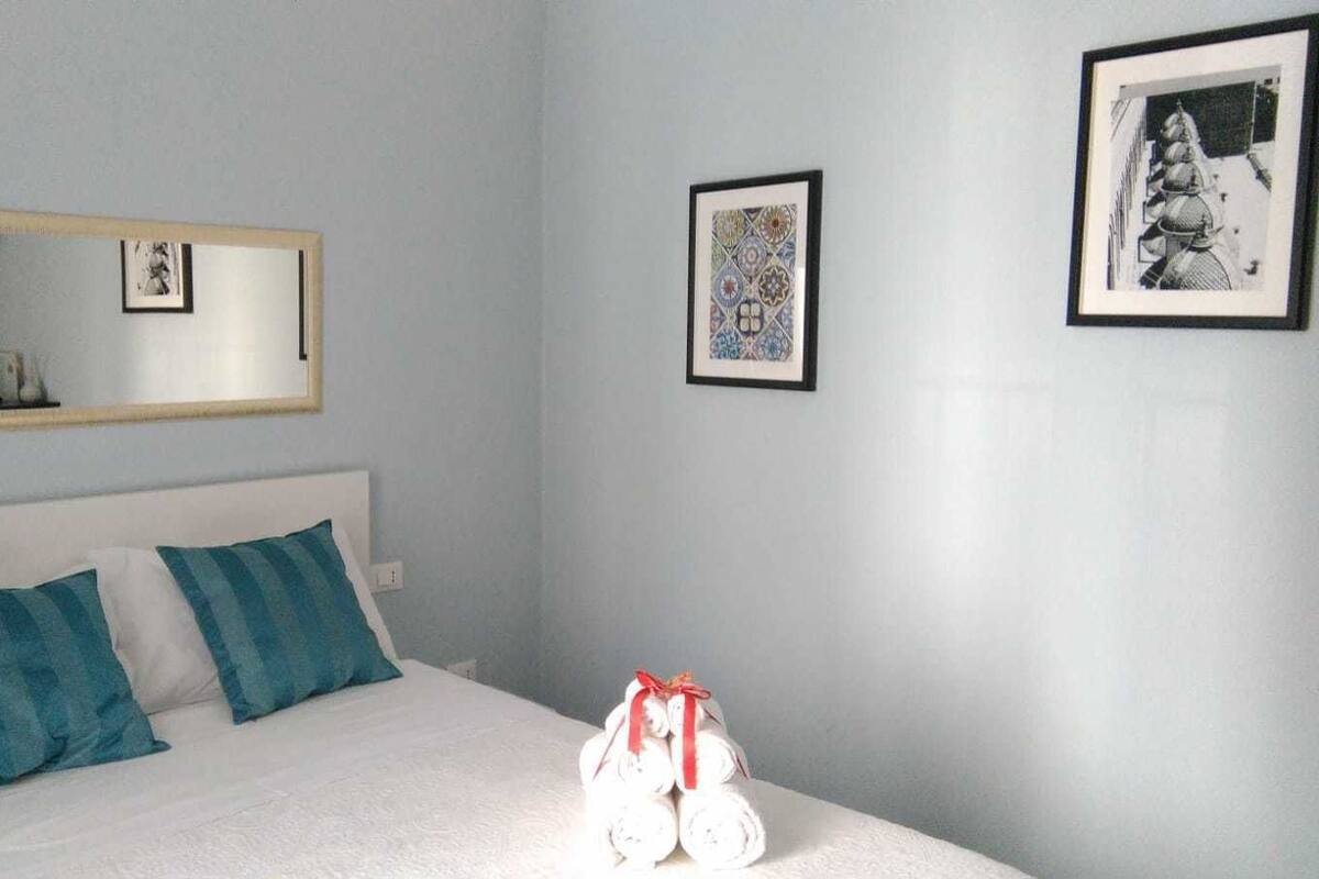 Ein Schlafzimmer mit einem Bett, zwei Kissen, einem Spiegel und zwei gerahmten Bildern an der Wand.