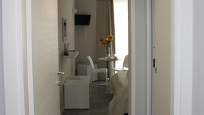 A narrow hallway leading to a bedroom with a bed, a chair, and a small table with flowers. - Triscele Glamour Rooms (Palermo)
