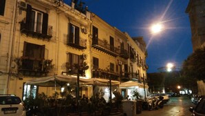 A street with outdoor seating at cafes, a parked car, and a building with balconies and windows. - Triscele Glamour Rooms (Palermo)